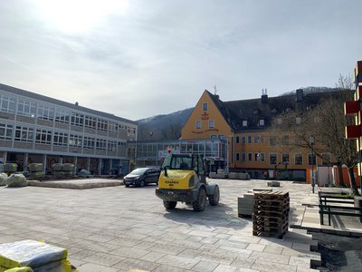 Baustelle mit einem gelben Radlader auf neu verlegten Pflastersteinen vor mehreren Gebäuden im Hintergrund